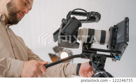 Cameraman work. Videographer production. Man adjusts professional filming device in light studio. Male cinematographer shooting process. 122246735