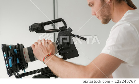 Photographer focus. Cameraman work. Man looks at display professional filming equipment tripod. Videographer setting studio production device. 122246767