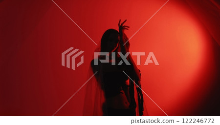 Female dance. Movement therapy. Relaxed woman silhouette in trance wearing polyethylene rags performing graceful hand activity isolated on dark red glow copy space background. 122246772