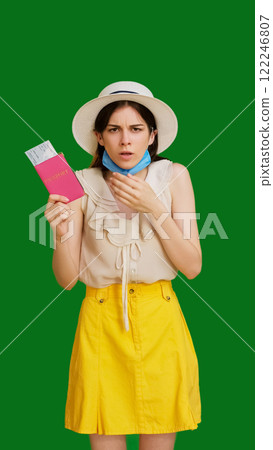 Shocked traveler woman in protective mask holding passport with tickets showing concern isolated on green copy space background. 122246807