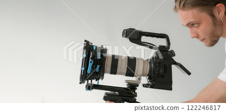 Videographer work. Studio cameraman. Man looks into lens professional camera. Male operator directs video recording tripod equipment. 122246817
