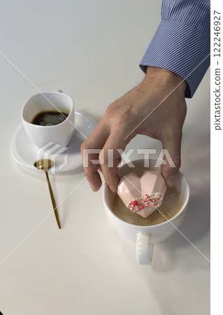 male hand lowers a soft pink heart with coffee marshmallows, sweets into the coffee 122246927