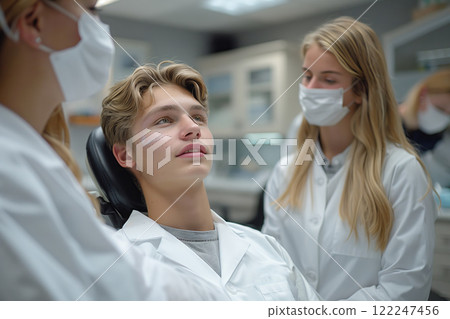 Young man in dental chair with two dentists in white coats Young man in dental chair with two dentists in white coats 122247456