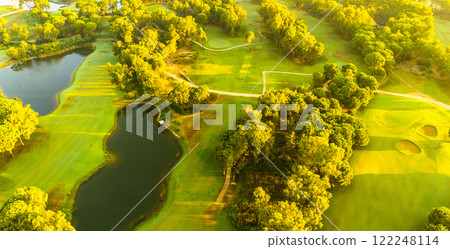 An aerial view of a golf course with ponds, winding paths, and vibrant greenery bathed in golden light An aerial view of a golf course with ponds, winding paths, and vibrant greenery bathed in golden light 122248114