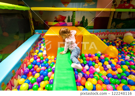 A child exploring soft play structures in a colorful ball pit at a vibrant indoor playground. 122248116