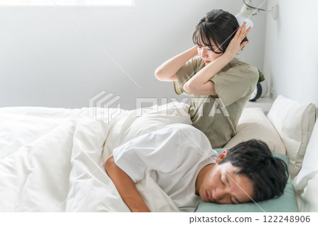 A wife who is sleep deprived because of her husband's snoring and sleep talking in bed. 122248906