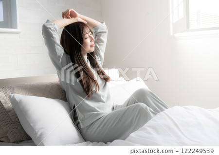 A woman stretching and waking up in bed 122249539