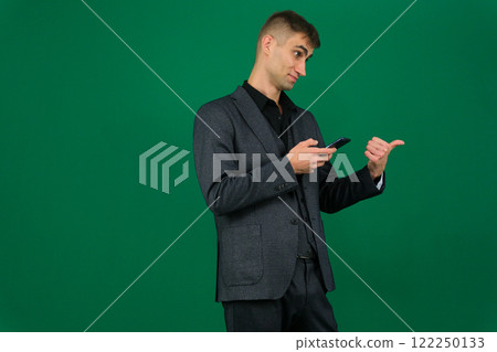 emotions of a handsome man guy on a green background chromakey close-up dark hair young man. phone in hand talk dial SMS online call gadget boss work advertising 122250133