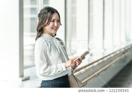 Smiling woman using a smartphone in the station lobby (app/mobile ticket/ticketless/electronic ticket) Smiling woman using a smartphone in the station lobby (app/mobile ticket/ticketless/electronic ticket) 122250541