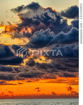 In the picture of a sunset over the sea: the orange horizon smoothly turns into dark silhouettes of clouds, the reflection of a warm glow on the surface of the water. 122250933