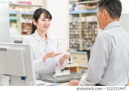 A female pharmacist and an elderly man explaining medicines at the pharmacy cash register 122251447