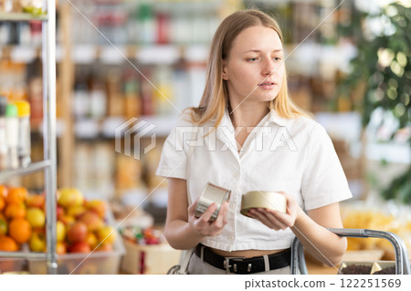 Young woman choosing canned food in grocery store 122251569