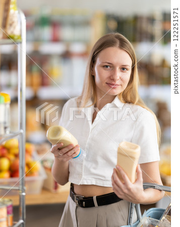 Choose food in supermarket - woman chooses mayonnaise to buy in the grocery department section of store 122251571