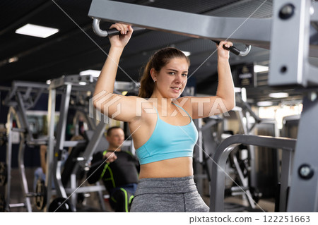 Girl training back muscles in lat pull-down lever machine Girl training back muscles in lat pull-down lever machine 122251663