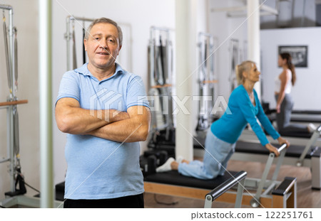 Portrait of positive mature man in sportswear smiling at camera before workout in Pilates rehabilitation center Portrait of positive mature man in sportswear smiling at camera before workout in Pilates rehabilitation center 122251761