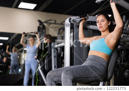 Sporty young woman using overhead press machine in gym 122251773