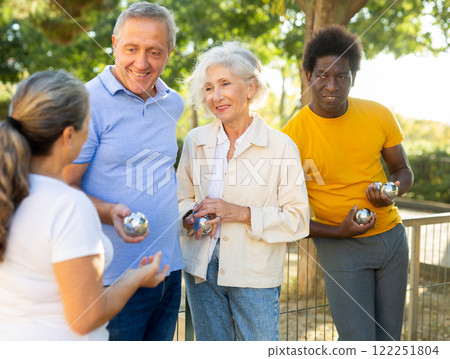 Cheerful group of multiracial mature adult people standing together and talking during a break in petanque game outside at park Cheerful group of multiracial mature adult people standing together and talking during a break in petanque game outside at park 122251804