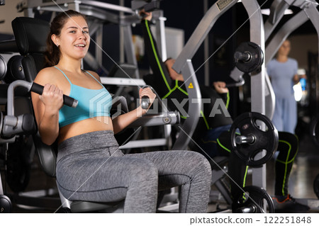 Smiling girl doing bicep curls on gym machine 122251848