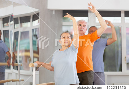 Elderly women and men practice at ballet standing in fourth position at barre in choreography studio 122251850