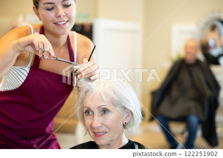 Elderly lady getting haircut by professional female hairdresser using scissors 122251902