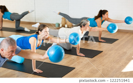 Middle-aged woman practicing pilates with ball in gym area Middle-aged woman practicing pilates with ball in gym area 122251941
