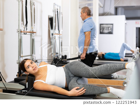 Young sporty woman doing Pilates exercise or side stretching to tone muscles on performer in studio Young sporty woman doing Pilates exercise or side stretching to tone muscles on performer in studio 122251943
