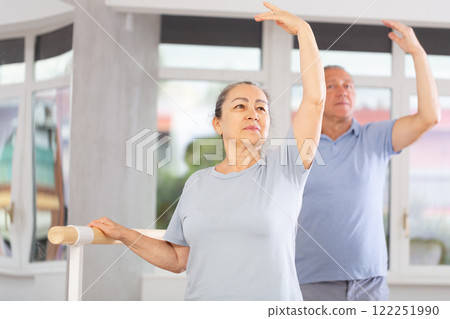 Elderly women and men practice at ballet standing in fourth position at barre in choreography studio 122251990