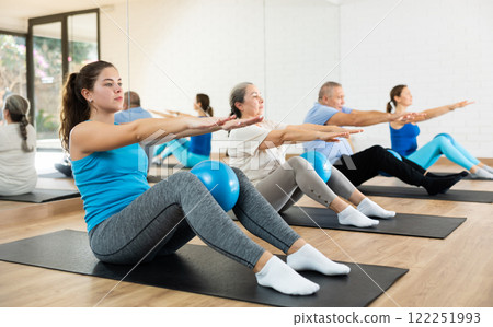Group of young elderly people in sportswear exercising Pilates with mini balls while lying on mats in rehabilitation center Group of young elderly people in sportswear exercising Pilates with mini balls while lying on mats in rehabilitation center 122251993