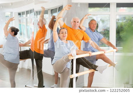 Dedicated mature females and males ballet dancer performing leg stretch at barre with concentration and grace in choreography studio during group rehearsal Dedicated mature females and males ballet dancer performing leg stretch at barre with concentration and grace in choreography studio during group rehearsal 122252005