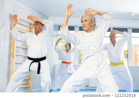Old woman attendee of karate classes practicing kata standing in row with others Old woman attendee of karate classes practicing kata standing in row with others 122252018