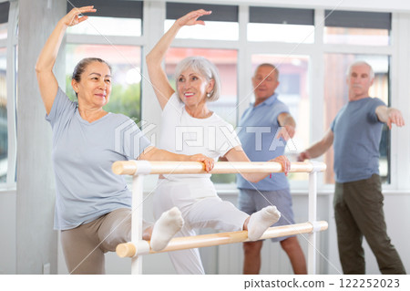 Two mature women practicing leg stretching exercise during ballet classes 122252023