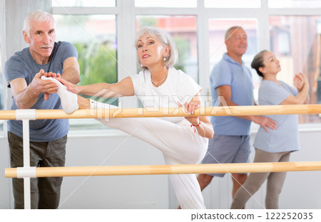 Male choreographer teaches elderly ballet lovers to stand in grand batman position 122252035