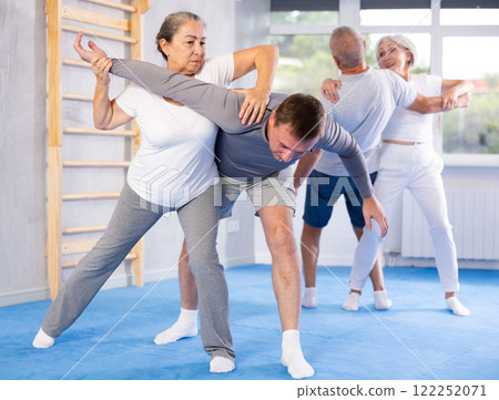 Senior woman in pair with middle-aged coach train Krav Maga and self-defense skills. Senior woman in pair with middle-aged coach train Krav Maga and self-defense skills. 122252071