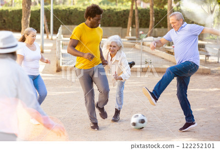 Excited elderly multiracial people playing street football on the playground on a sunny weather 122252101