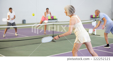 Sportive slim woman with racquet playing pickleball in court. View from back 122252121