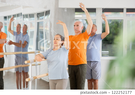 Active mature woman practicing third position holding by ballet barre together with others Active mature woman practicing third position holding by ballet barre together with others 122252177