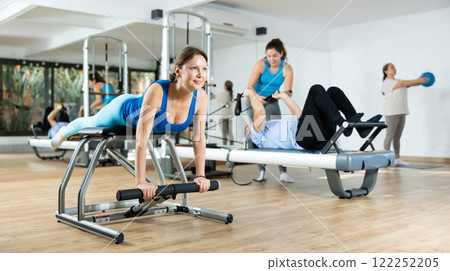 Middle-aged woman practicing pilates on pedal fitness chair in sports hall 122252205