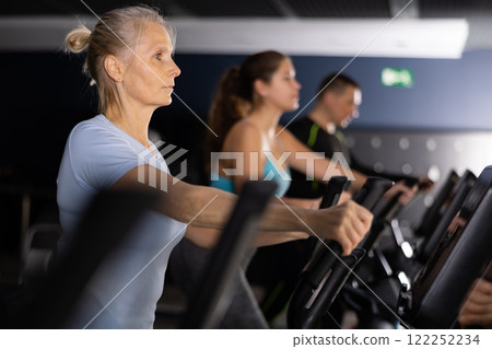 Elterly woman in sportswear doing cardio training on ellipsoid in gym 122252234