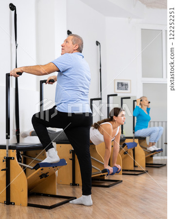 Mature man performing standing Pilates exercise on Wanda chair in fitness studio Mature man performing standing Pilates exercise on Wanda chair in fitness studio 122252251