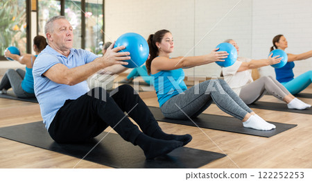 Group of young elderly people in sportswear exercising Pilates with mini balls while lying on mats in rehabilitation center 122252253