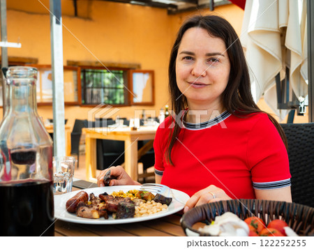 Portrait of woman spending time on open terrace of restaurant and eating traditional parillada de carne 122252255