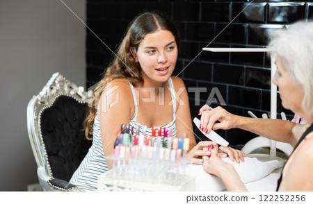 Girl client of beauty salon gave hand to blurry manicurist senior woman and enjoys having manicure 122252256