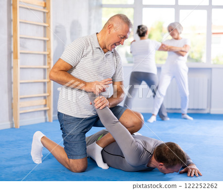 Self defense lesson - elderly man twists the arm of attacking man with painful hold in gym Self defense lesson - elderly man twists the arm of attacking man with painful hold in gym 122252262