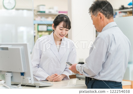 A woman who is a pharmacist/dispenser explaining a smartphone app to elderly/middle-aged men at a pharmacy (medication guidance) A woman who is a pharmacist/dispenser explaining a smartphone app to elderly/middle-aged men at a pharmacy (medication guidance) 122254038