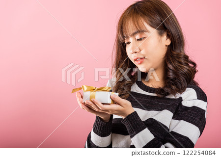 Portrait of happy beautiful Asian young woman smiling holding small gift box on hands, studio shot isolated on pink background, gift for you. Birthday, New year, Christmas, valentine day concept Portrait of happy beautiful Asian young woman smiling holding small gift box on hands, studio shot isolated on pink background, gift for you. Birthday, New year, Christmas, valentine day concept 122254084