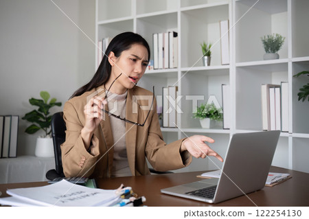 Unhappy Asian business woman shows stress over unsuccessful business while working in home office decorated with soothing green plants. 122254130