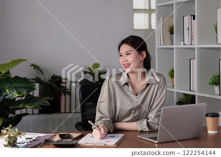 Young Asian business woman sitting in the office using a calculator to calculate business numbers. Young Asian business woman sitting in the office using a calculator to calculate business numbers. 122254144