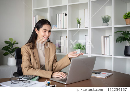 Young Asian business woman sits and works using a laptop in a modern office decorated with shady green plants. Young Asian business woman sits and works using a laptop in a modern office decorated with shady green plants. 122254167