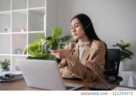 Unhappy Asian business woman shows stress over unsuccessful business while working in home office decorated with soothing green plants. Unhappy Asian business woman shows stress over unsuccessful business while working in home office decorated with soothing green plants. 122254173