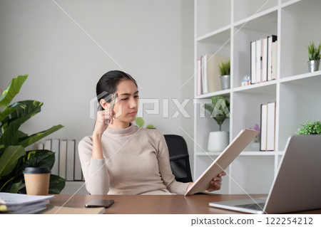 Asian businesswoman who is tired and has a headache from difficult work causing stress Sitting and looking at work at the desk in the office. 122254212